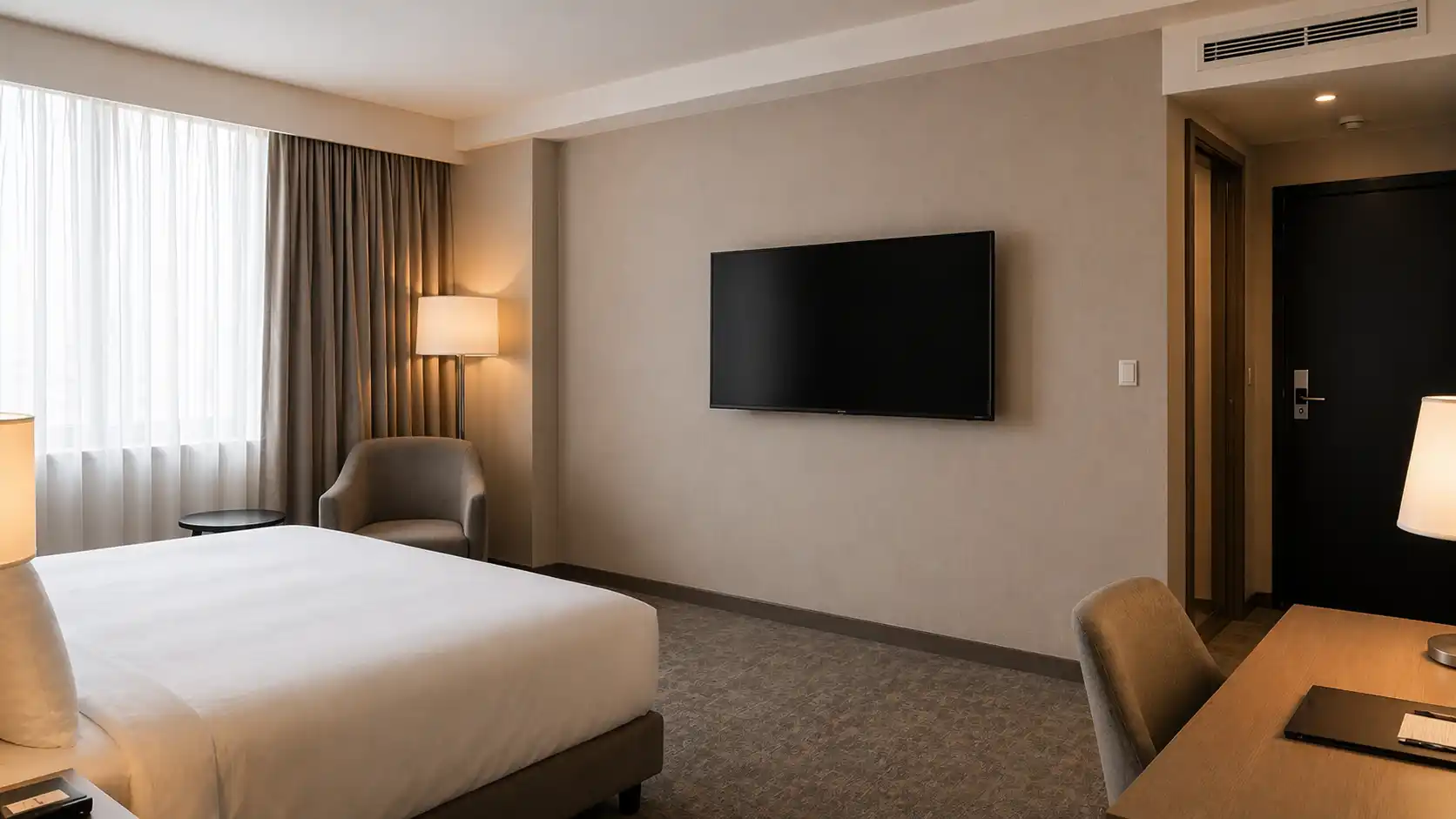 Telewizor hotelowy zamontowany bezpośrednio na ścianie naprzeciw łóżka