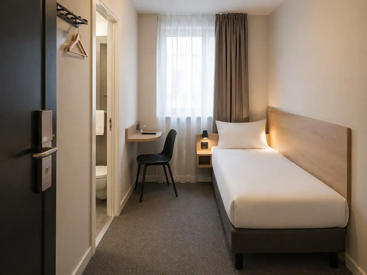 Bardzo mały pokój hotelowy z pojedynczym łóżkiem, małym blatem i podstawowym wyposażeniem