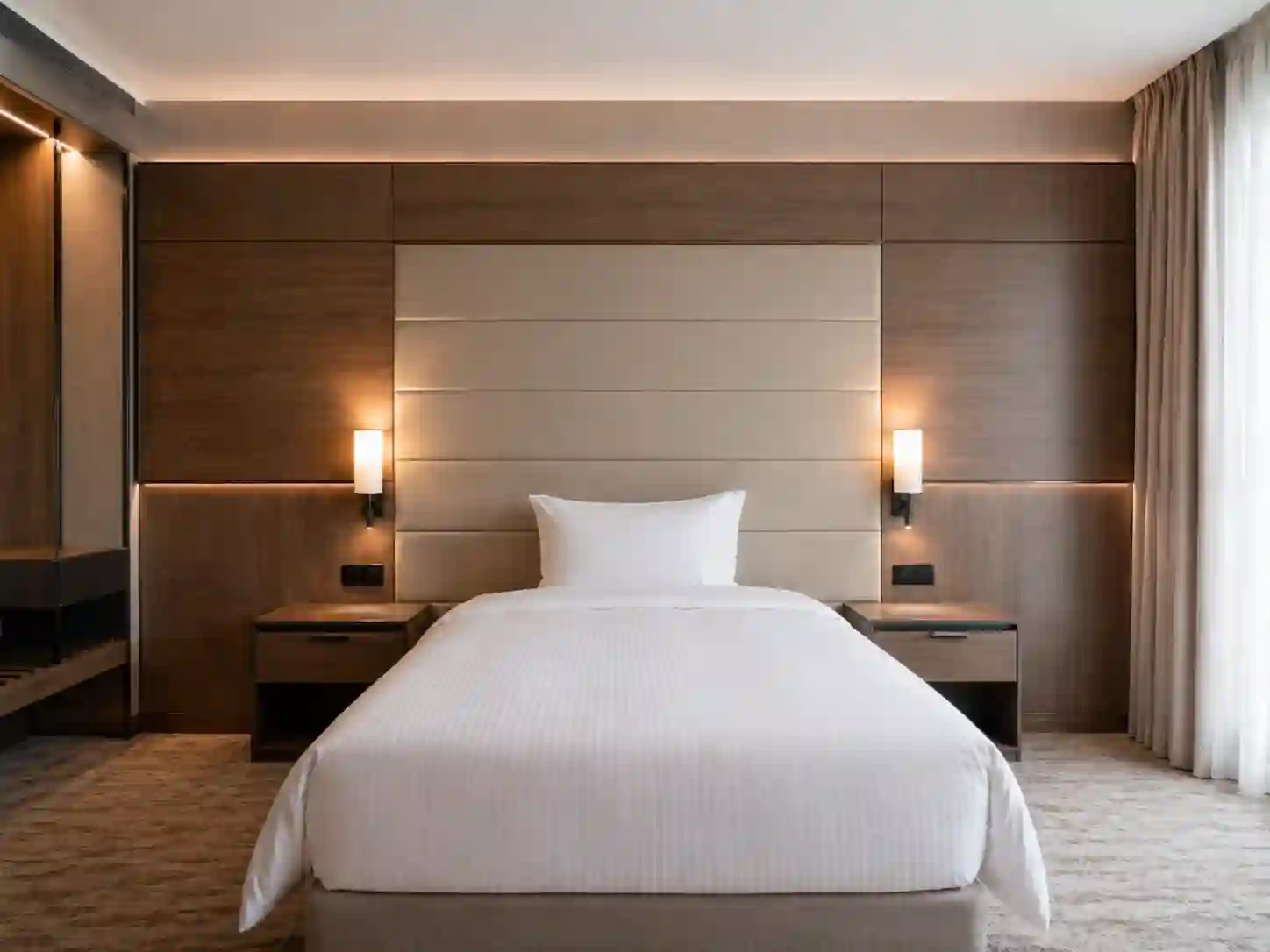 Szeroka ściana panelowa za łóżkiem hotelowym z oświetleniem i stolikami nocnymi