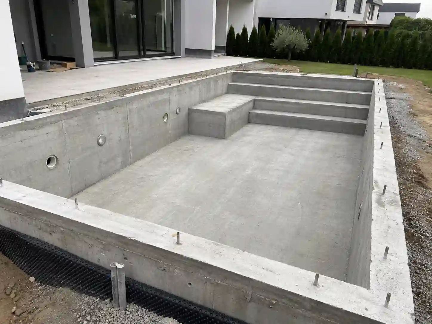 Niecka basenu żelbetowego przed wykończeniem z betonowymi schodami i przejściami instalacyjnymi