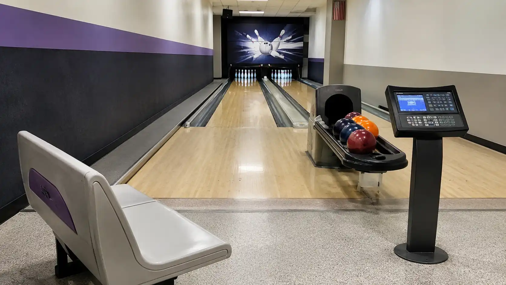 Prosta strefa gracza przy torze bowlingowym z ławą, kulami i panelem obsługi