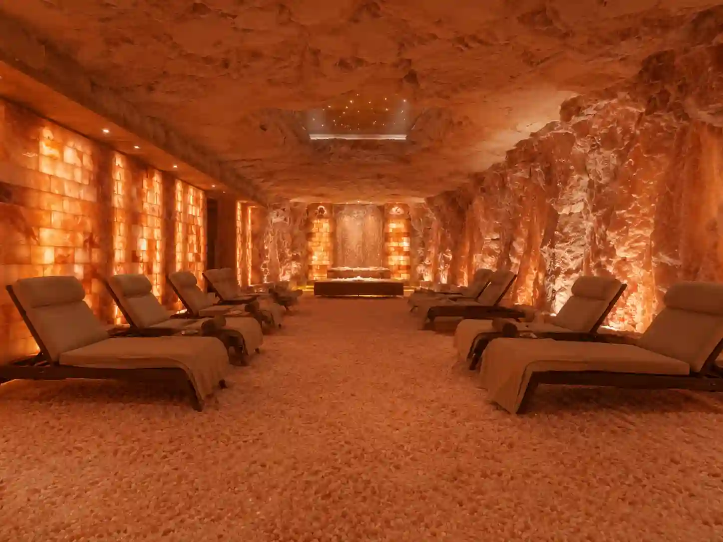 Pełna grota solna z kilkoma leżakami, ścianami z cegieł solnych i podłogą pokrytą granulatem.