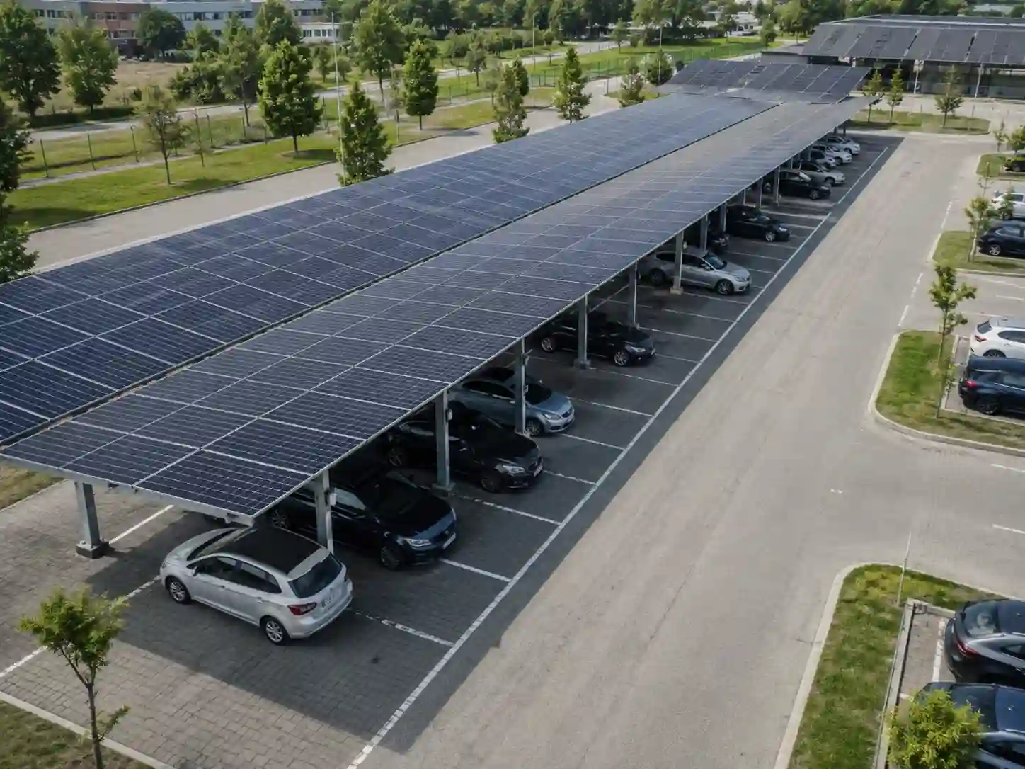 Wielostanowiskowa wiata fotowoltaiczna nad parkingiem z długimi rzędami modułów i kilkunastoma samochodami.