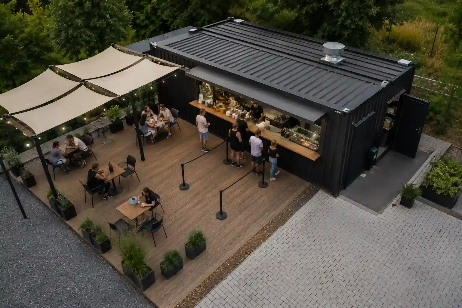 Kontener gastronomiczny z naziemnym tarasem, pergolą i stolikami dla klientów.