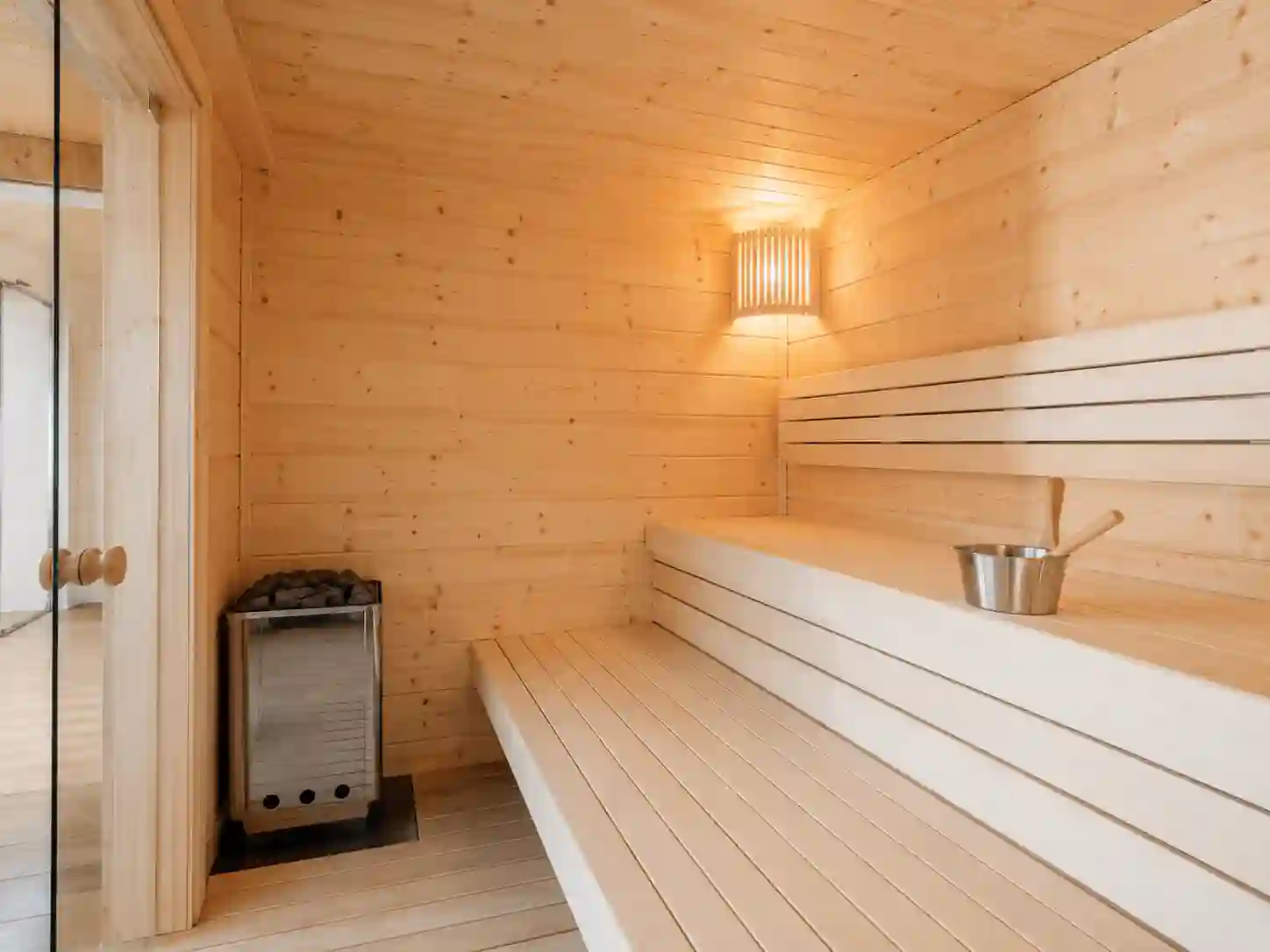 Jasna sauna fińska wykończona świerkiem i osiką z prostymi dwupoziomowymi ławkami.